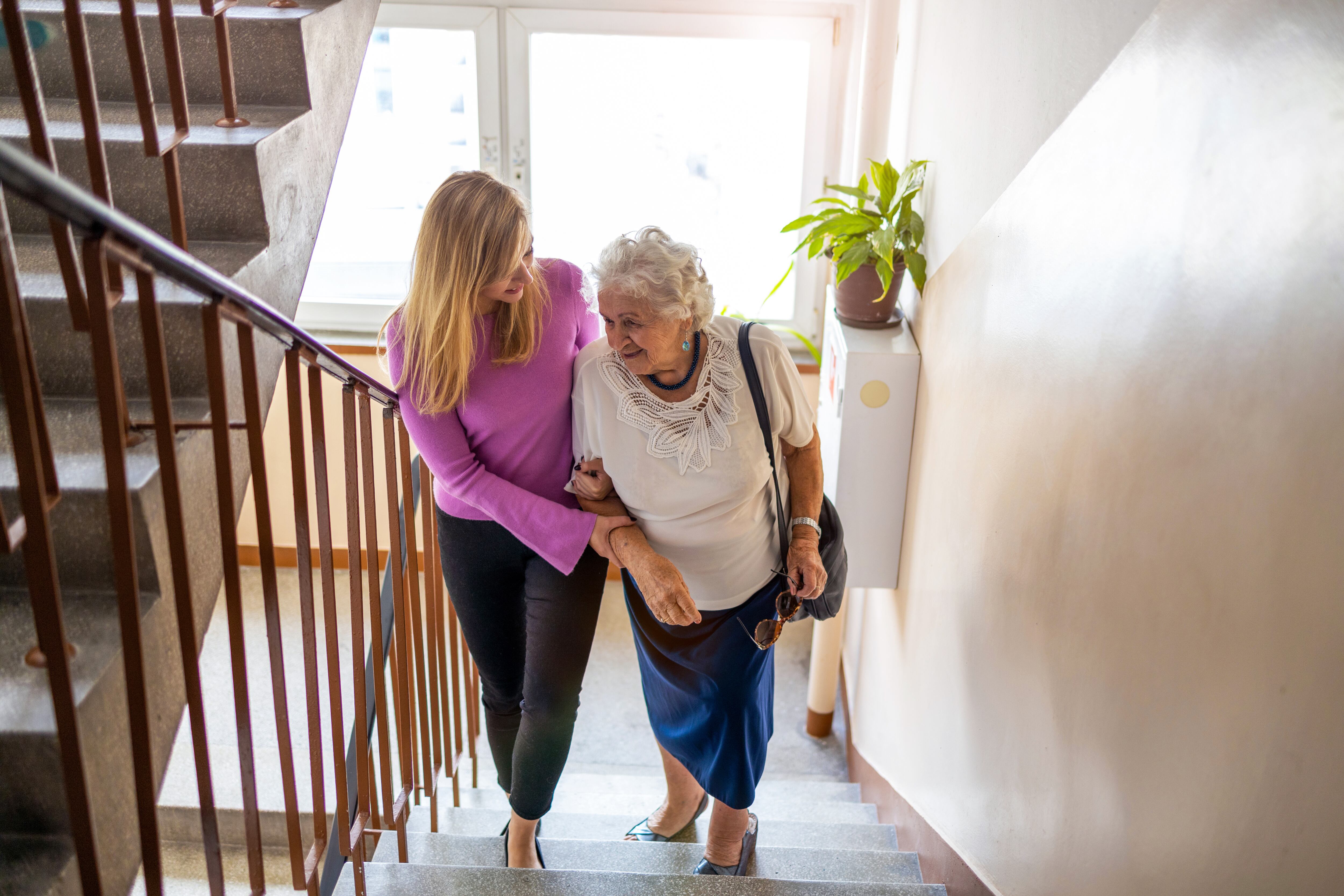 Una mujer ayudando a una persona mayor a subir las escaleras (AdobeStock)