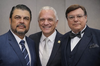 Primer plano de tres hombres vestidos formalmente. Uno lleva traje azul, otro traje oscuro con corbata clara, y el tercero esmoquin y pajarita.