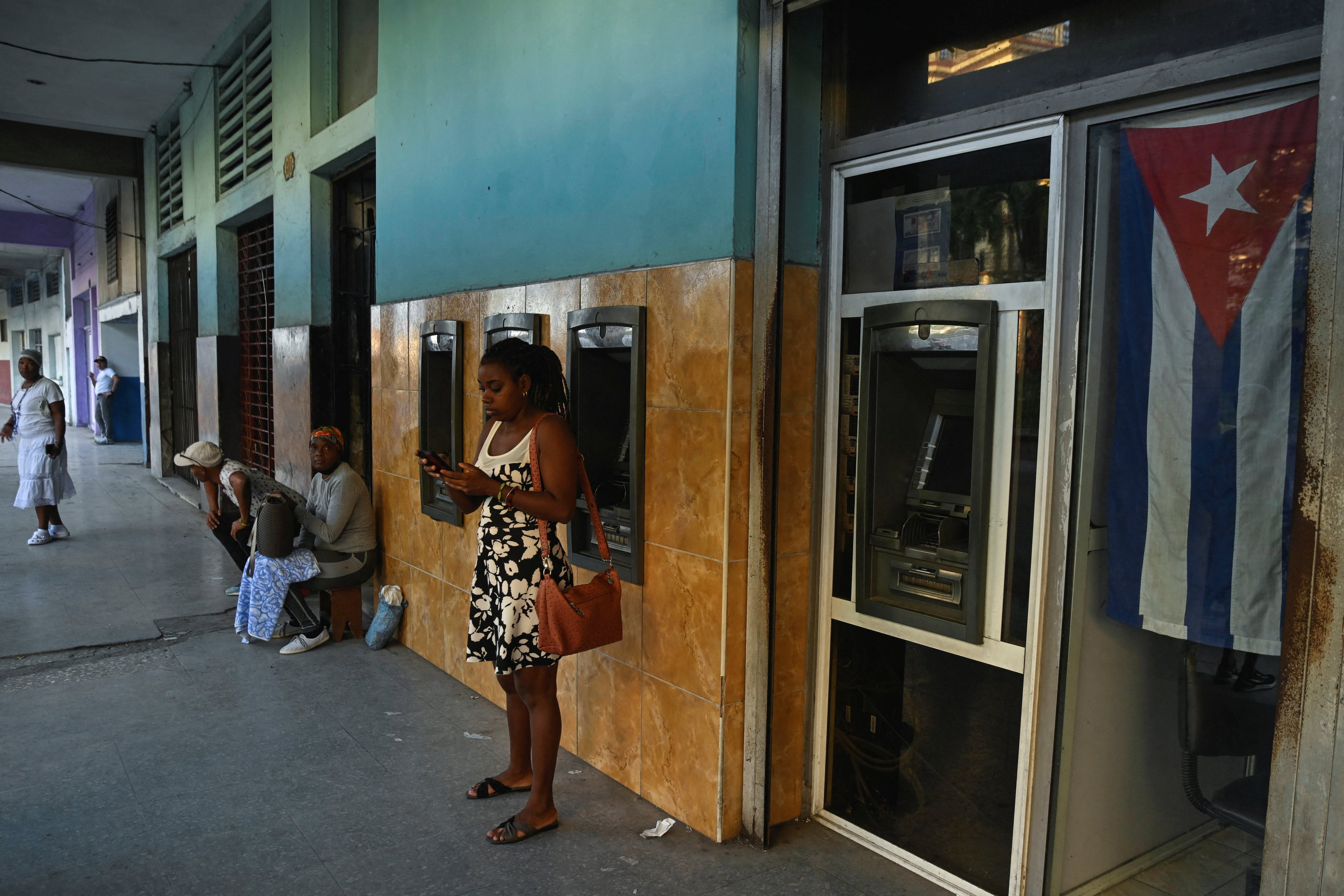 Una mujer usa su teléfono móvil frente a un banco en medio de un colapso parcial de la red eléctrica en La Habana, Cuba, el 3 de diciembre de 2025. La población que recibe remesas no puede sacar el dinero porque los cajeros no funcionan. REUTERS/Norlys Pérez