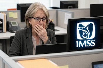 Una mujer con gafas, con la mano sobre la boca, mira fijamente una pantalla de computadora que muestra un logo blanco del IMSS.