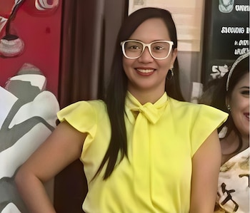 Primer plano de la jueza Alejandra Romero, una mujer de cabello oscuro y gafas blancas, sonriendo a la cámara y vistiendo una blusa amarilla con lazo