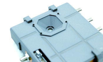 Vista en primer plano de un dispositivo plástico gris con una ranura hexagonal, un sensor en el centro y conectores metálicos
