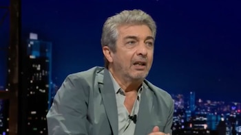 Ricardo Darín, hombre de mediana edad con cabello gris y barba, viste camisa gris y chaqueta verde, hablando en un programa de televisión nocturno