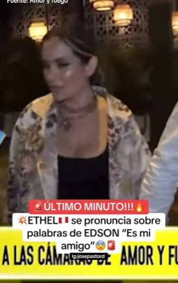 Ethel Pozo, con cabello castaño claro y un collar de cadenas, lleva una chaqueta estampada y un top negro, de pie en un lugar con luces tenues