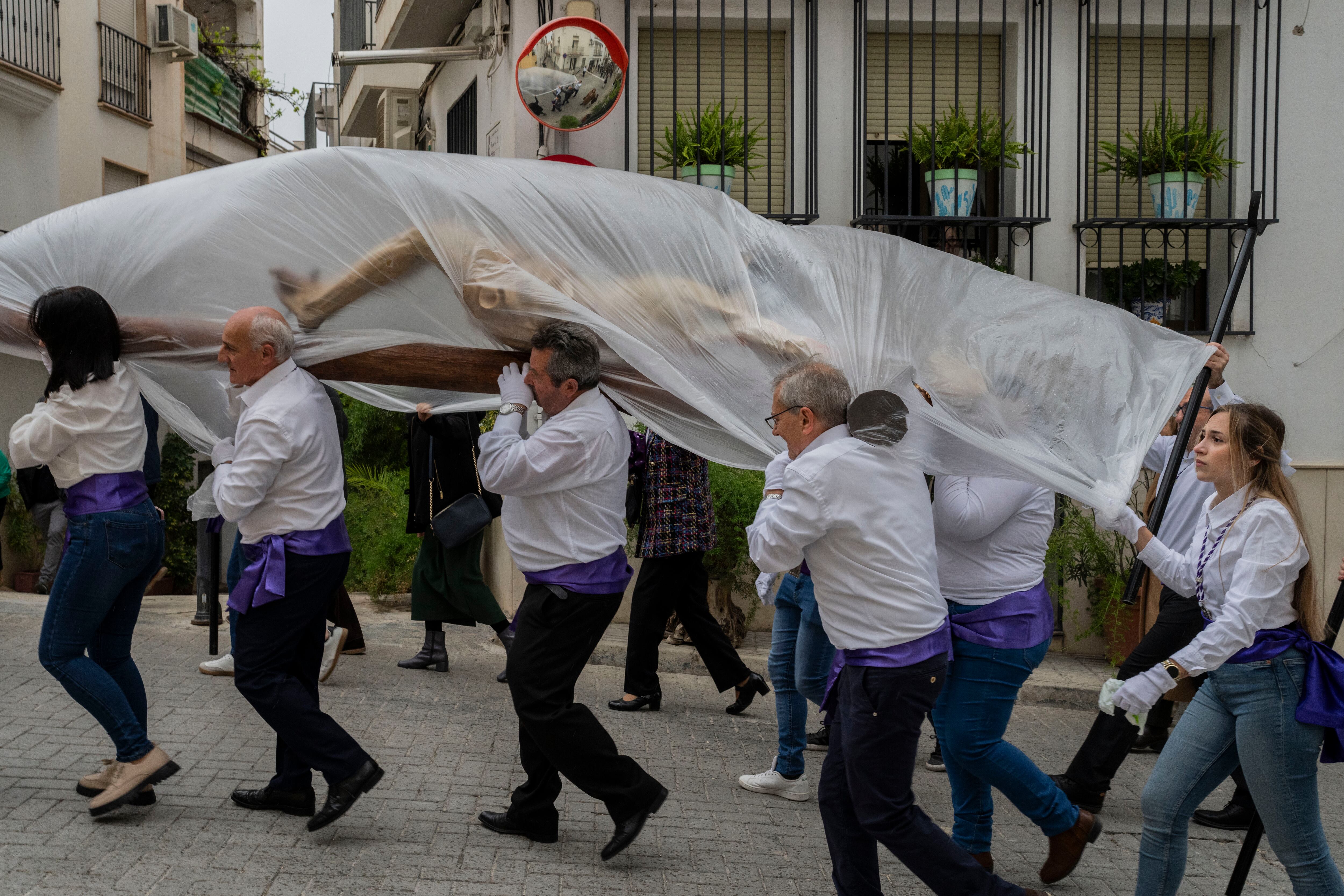 Miembros de la hermandad católica de Vera Cruz portan una talla de Jesucristo, cubierta por un plástico para protegerla de la lluvia, durante una procesión de Semana Santa en Quesada, Jaén, el viernes 29 de marzo de 2024. (AP/Bernat Armangue)
