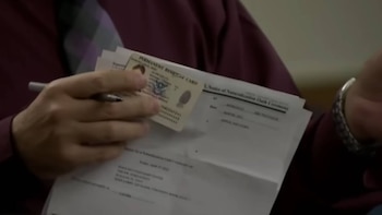 Primer plano de una mano sosteniendo una Tarjeta de Residente Permanente y documentos oficiales, incluyendo una notificación de ceremonia de juramento de naturalización