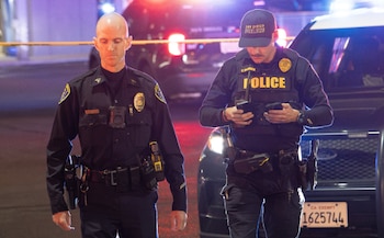 Dos oficiales de la Policía de San Diego caminan junto a un patrullero de noche; uno de ellos revisa dos teléfonos móviles