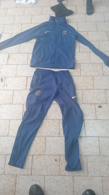 Un conjunto deportivo azul oscuro, que incluye una chaqueta con el logo del PSG y pantalones, tendido sobre un suelo de baldosas claras