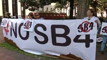 Personas sostienen una pancarta blanca grande con letras negras que leen '#NOSB4' y varios carteles más pequeños que muestran 'SB4' tachado