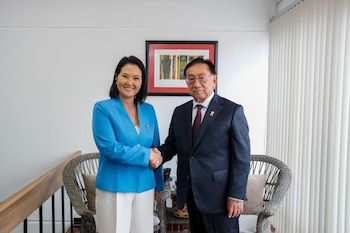 Keiko Fujimori y José María Balcázar, vestidos con traje formal, se dan la mano frente a una pared blanca con un cuadro y unas persianas verticales