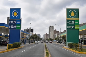 Dos carteles de precios de combustible a los lados de una avenida muestran valores de diésel y gasohol con el símbolo de soles.