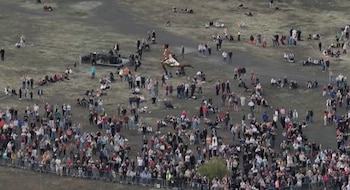 Vista aérea de una multitud reunida en un campo abierto observando a una persona caminando sobre un cable suspendido