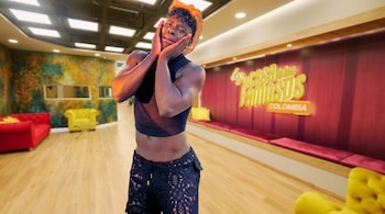 Campanita, con sombrero, blusa transparente negra y pantalones de encaje, se lleva las manos a la cara con expresión de llanto en un estudio de televisión.