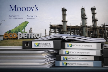 Pila de carpetas y papeles de Moody's Corporation en primer plano, con el logo de Moody's y una planta petrolera de Ecopetrol de fondo.