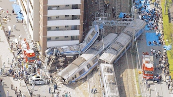 Vista aérea de un grave descarrilamiento de tren en Amagasaki, Japón, mostrando varios vagones volteados, personal de rescate y bomberos en el lugar del accidente