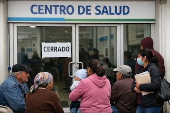 Grupo de personas, incluyendo niños y adultos mayores, sentadas o de pie frente a la puerta de un Centro de Salud con un cartel de 'Cerrado'.