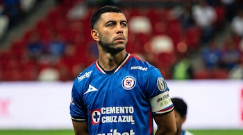 Un jugador de fútbol viste una camiseta azul con logotipos impresos y una cinta de capitán en el brazo.