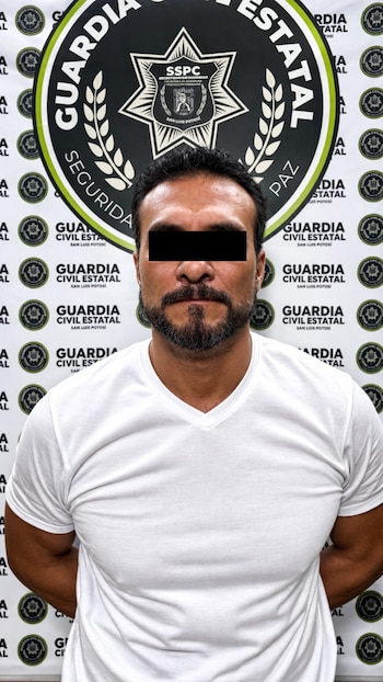 Un hombre con barba y bigote, vestido con una camiseta blanca, posa frente a un fondo blanco con logos repetidos de la Guardia Civil Estatal