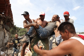 Varios vecinos trasladan a un hombre rescatado de entre los escombros de un edificio derrumbado, un día después de dos sismos, el jueves 25 de junio de 2026, en La Guaira, Venezuela (AP Foto/Pedro Mattey)