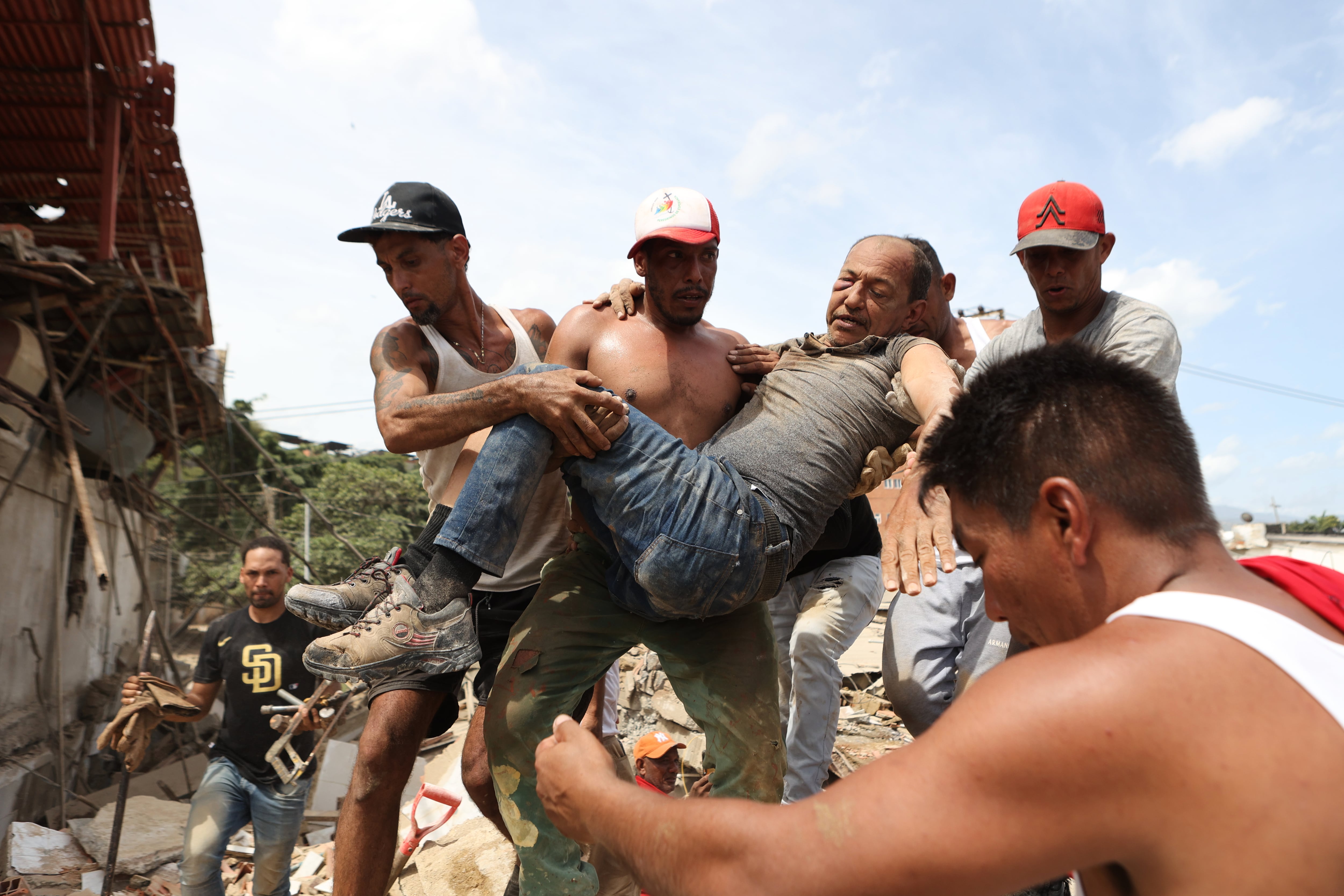 Varios vecinos trasladan a un hombre rescatado de entre los escombros de un edificio derrumbado, un día después de dos sismos, el jueves 25 de junio de 2026, en La Guaira, Venezuela. (AP Foto/Pedro Mattey)