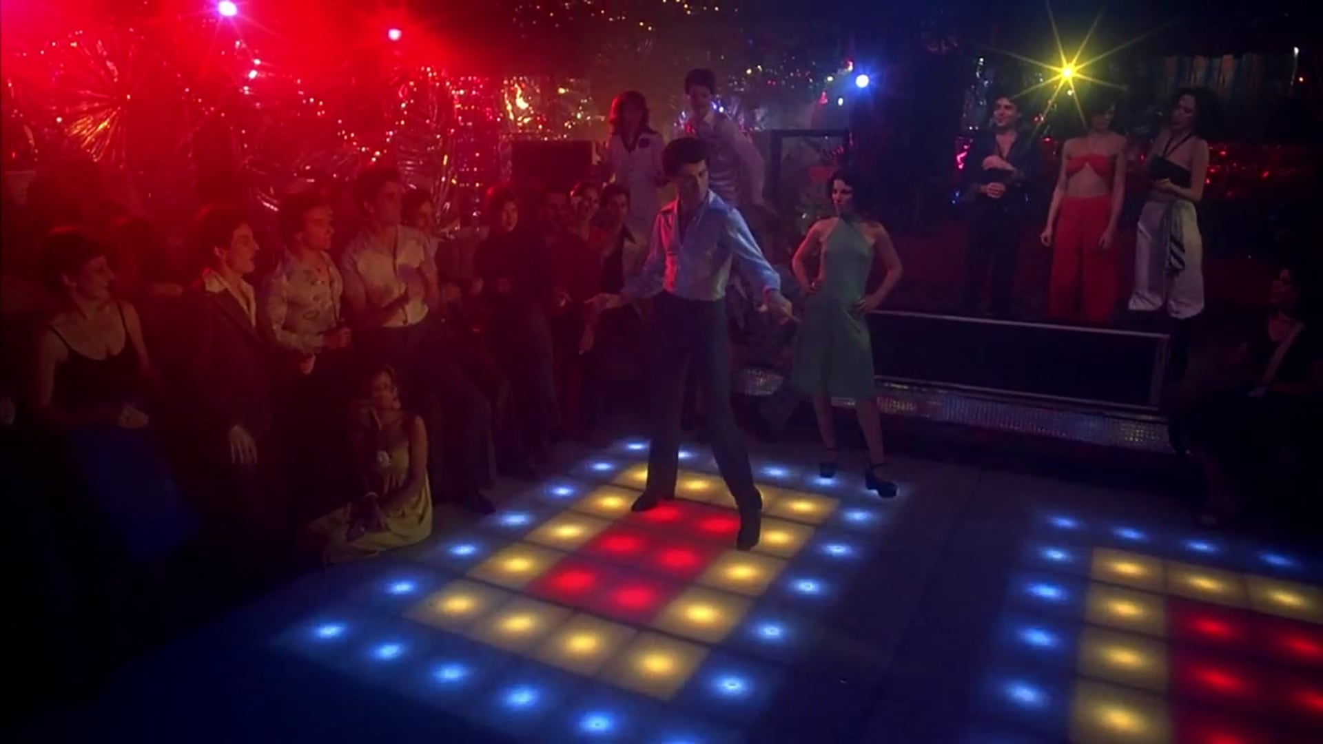 La legendaria pista de baile de Fiebre de sábado por la noche cobra vida con el protagonista Tony Manero bailando entre las luces de neón en un vibrante club nocturno. (Captura de video)