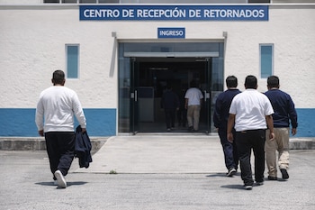Vista trasera de varios hombres ingresando a un edificio blanco con una franja azul y un letrero azul que dice 'CENTRO DE RECEPCIÓN DE RETORNADOS' y 'INGRESO'.