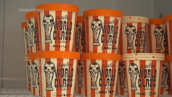 Múltiples botes de helado Betty Rae's Ice Cream "World Class Creations 2026" con rayas crema y naranja, apilados en un estante de refrigerador