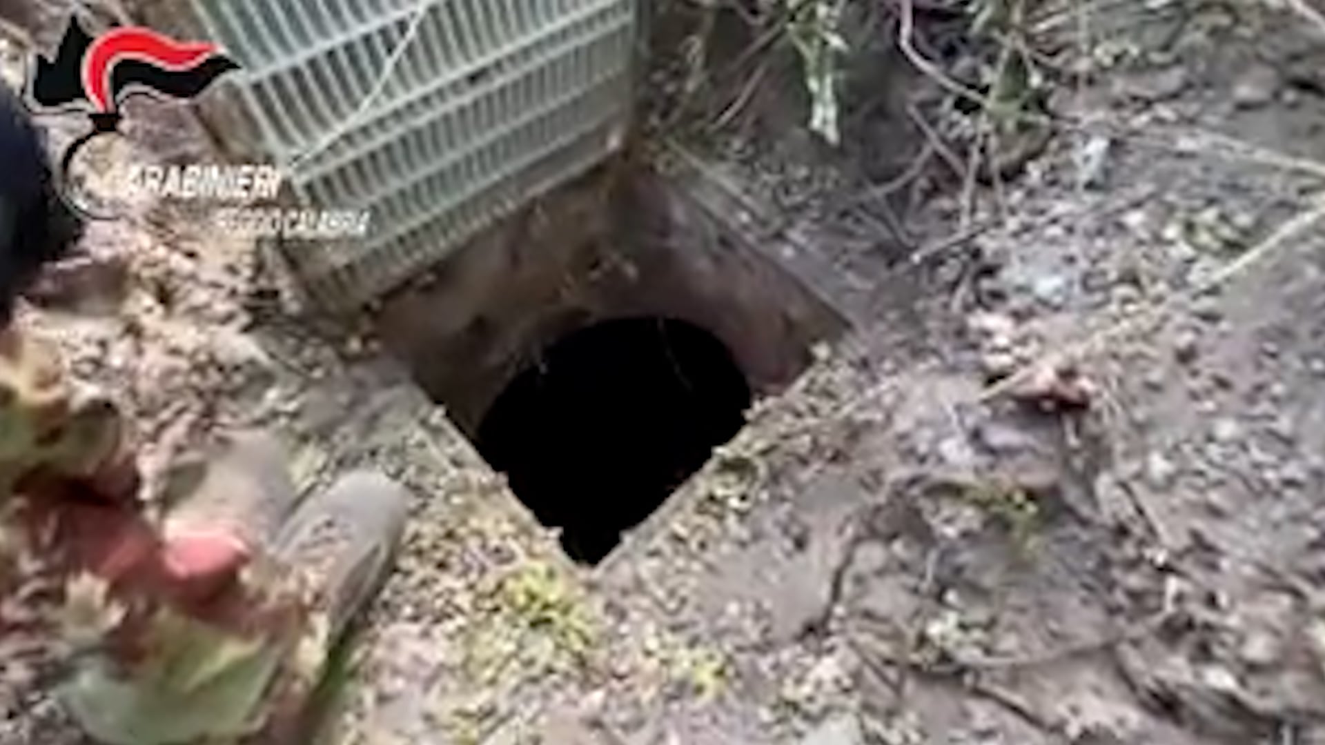 Carabinieri inspeccionan la entrada del túnel subterráneo del búnker de la 'Ndrangheta en Ardore, oculta bajo una rejilla metálica en el terreno, durante el operativo en Reggio Calabria. (Carabinieri)