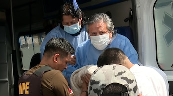 Alejandro Toledo con bata azul y mascarilla en una ambulancia, asistido por personal médico y un agente con chaleco marrón.