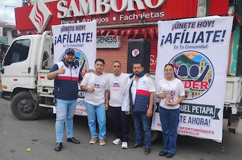 Cinco personas posan en la calle junto a dos pancartas publicitarias de afiliación colocadas frente a un camión blanco