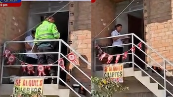 Entrada de edificio de ladrillo con escalera exterior y barandilla blanca, una oficial de policía, personas, cartel Se Alquila Cuartos y guirnaldas rojas