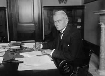 Retrato en blanco y negro del Senador Hiram Bingham, un hombre con cabello peinado hacia atrás, sentado en un escritorio escribiendo con una pluma