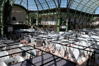 Vista aérea del interior del Grand Palais, con su techo de vidrio y estructuras verdes, sobre un gran número de stands de arte blancos y personas
