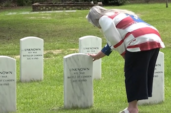 Uma mulher vestindo uma blusa com a bandeira americana tocando uma lápide branca com inscrições