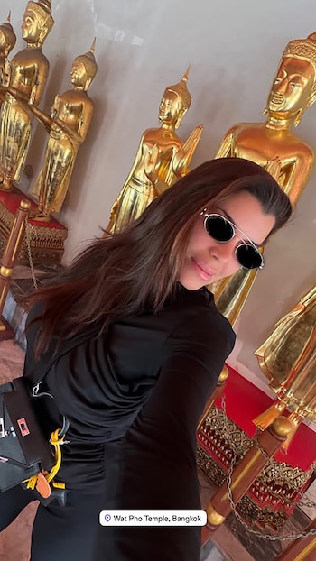 Una mujer con cabello oscuro y gafas de sol redondas sonríe, en primer plano, con varias estatuas doradas de Buda detrás de ella en el Templo Wat Pho