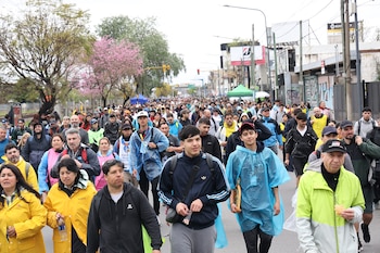 Multitud de personas caminando por una calle asfaltada con impermeables de colores, abrigos y árboles al fondo