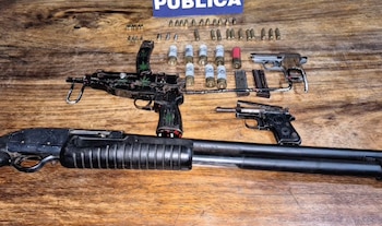 Una escopeta, un subfusil, dos pistolas, cargadores y diversos cartuchos y balas ordenados sobre una mesa de madera