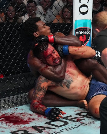 Un luchador aplica una llave al cuello de su oponente ensangrentado en la lona de un octágono de artes marciales mixtas