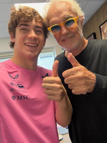 Franco Colapinto, con camiseta rosa, y Flavio Briatore, con gafas amarillas, posan sonrientes haciendo el gesto de pulgar arriba
