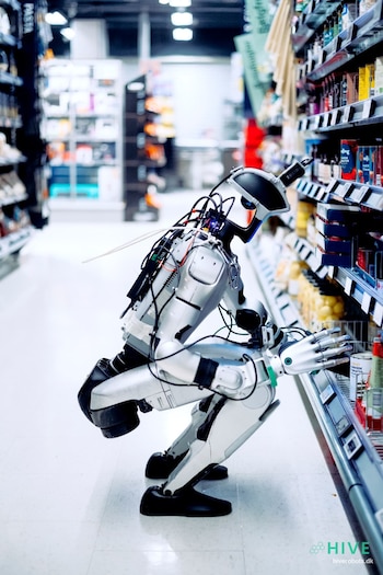 Un robot humanoide en cuclillas frente a una estantería llena de productos en el pasillo de un supermercado