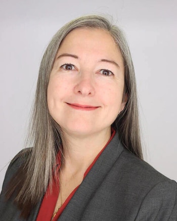 Plano medio de una mujer con cabello gris y castaño, chaqueta gris y blusa roja sobre un fondo claro