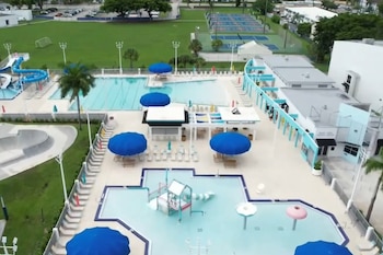 Vista aérea de un complejo recreativo con varias piscinas, toboganes de agua azules, un campo de fútbol, canchas de tenis y edificios