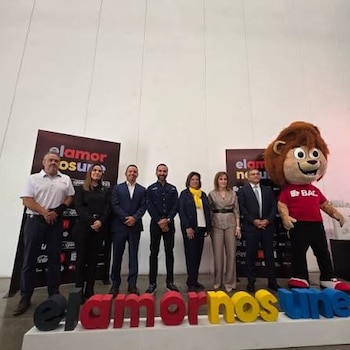 Siete personas y una mascota de león de peluche posan frente a dos pancartas y letras corpóreas que deletrean 'el amor nos une'