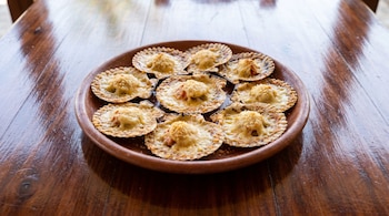 Plato circular de barro con nueve conchas gratinadas con queso, colocado sobre una mesa de madera oscura.