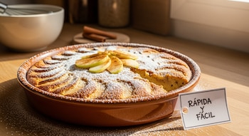 Budín de manzana y canela en un molde marrón con azúcar glas y rodajas de manzana. Una etiqueta dice 'Rápida y Fácil' en una cocina bien iluminada.