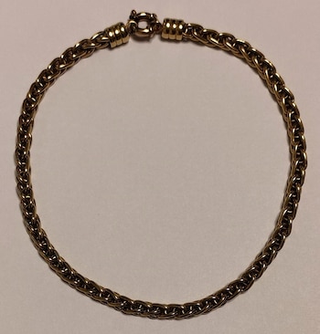 Pulsera dorada de eslabones entrelazados con un broche en la parte superior, colocada en círculo sobre un fondo claro