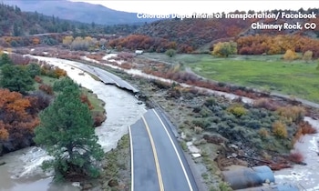 Vista aérea de una carretera asfaltada cortada transversalmente por el agua de un río entre vegetación y colinas