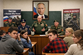 Una escena de un aula donde cuatro militares rusos hablan a estudiantes sentados en pupitres, con un retrato grande de Vladimir Putin colgado detrás.