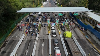 Vista aérea de una caseta de cobro carretero con personas concentradas en los carriles de paso y varios vehículos detenidos