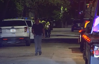 Un hombre camina de noche por una calle cerca de patrullas policiales y personal con chalecos reflectantes